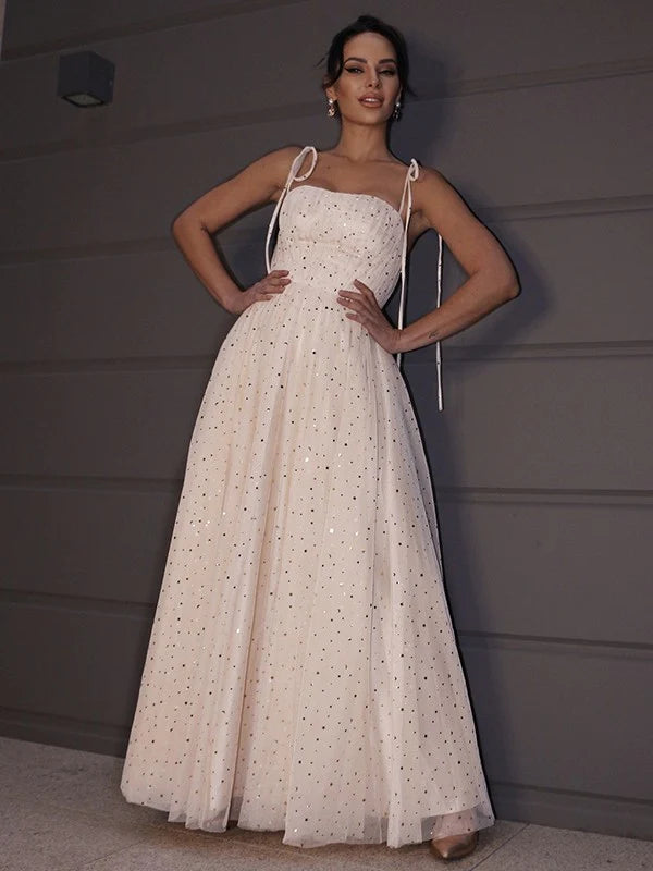 Woman wearing a sparkling A-line paillette spaghetti strap floor-length prom gown, front view.
