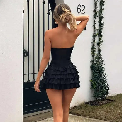 Model in a black strapless bodycon mini dress, showing the ruffled tiered skirt from a side angle.