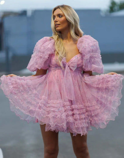 Model wearing a light blue A-line mini homecoming dress with puff sleeves, sweetheart neckline, floral print, and ruffles.