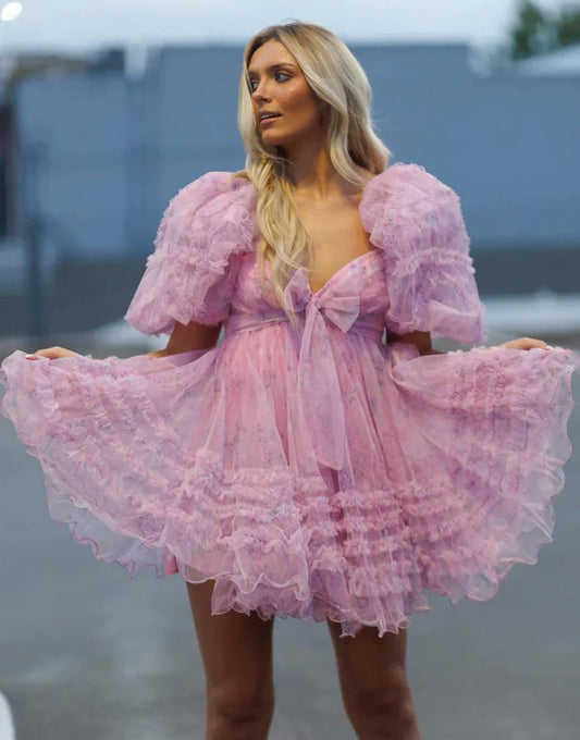 Model wearing a light blue A-line mini homecoming dress with puff sleeves, sweetheart neckline, floral print, and ruffles.