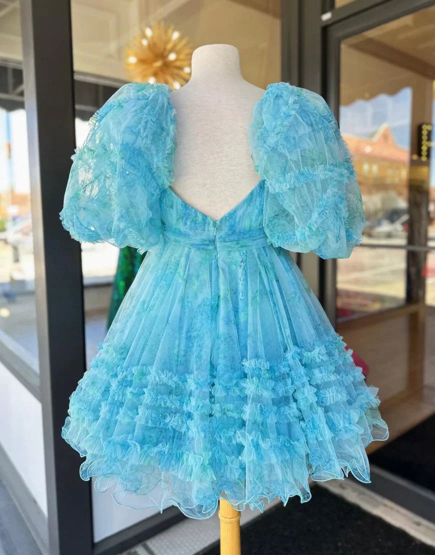 Back view of a model in a light blue floral A-line mini dress with puff sleeves and ruffles.