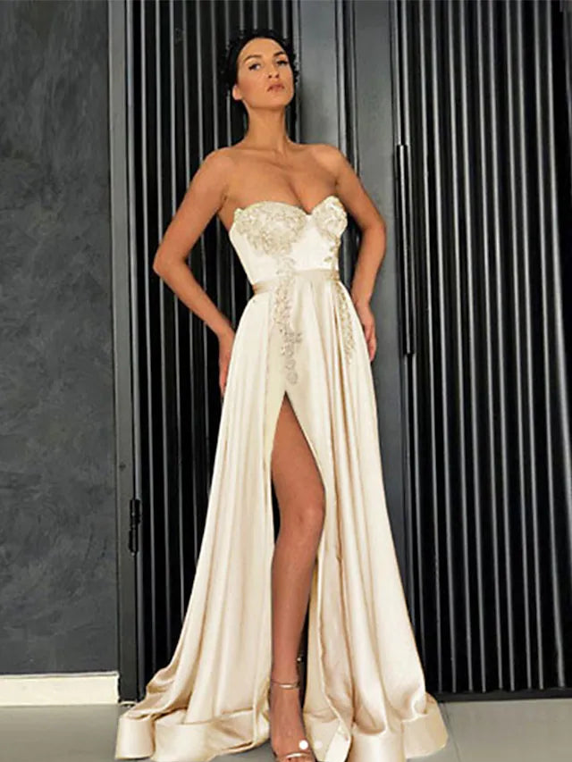 Woman posing in a light-colored A-line off-shoulder satin party dress with pleats and a slit.