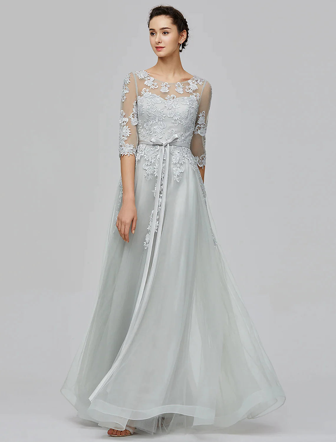 Woman wearing an elegant A-Line Empire tulle dress with illusion neck and half sleeves, front view.