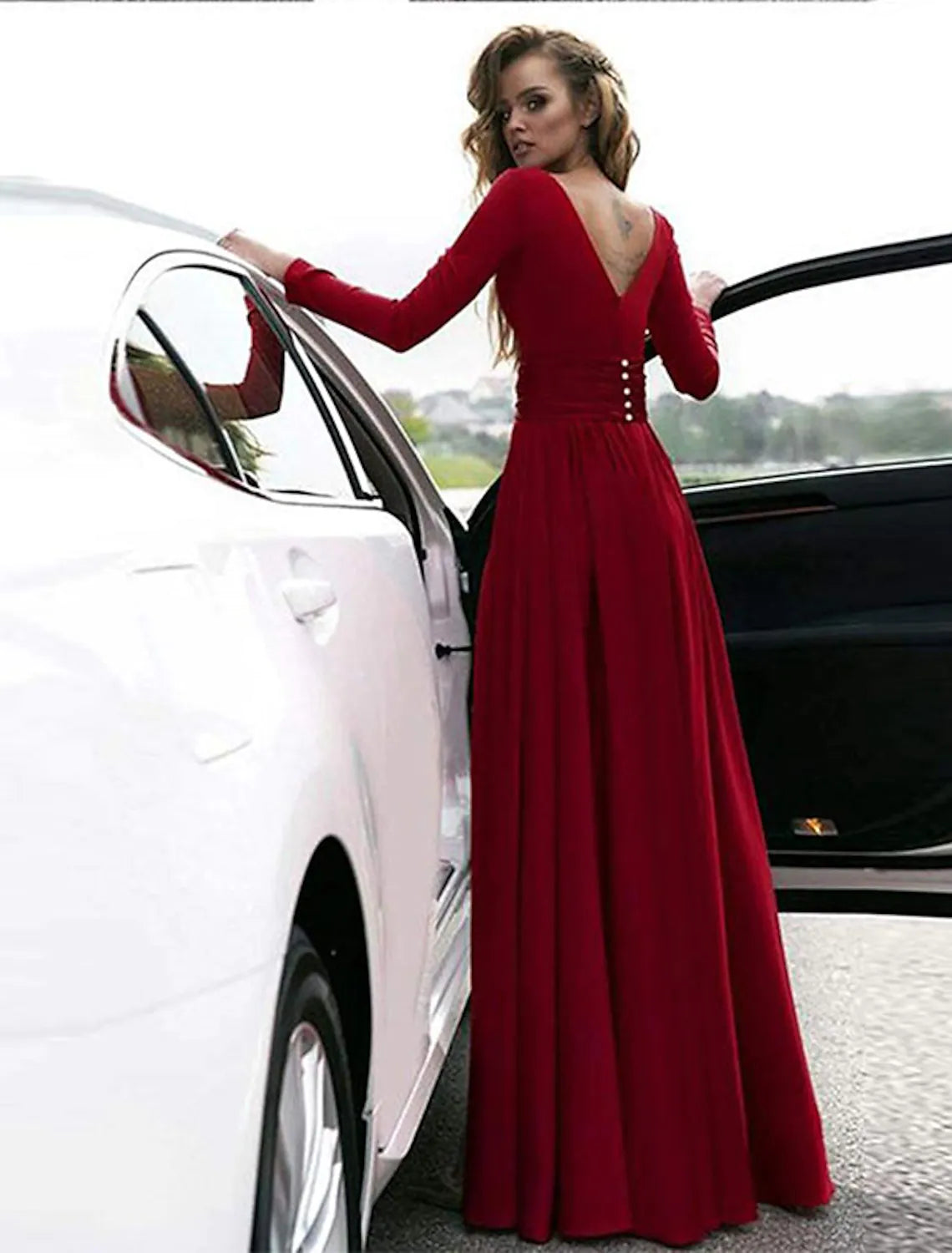 Back view of a woman in a pure color A-line empire long sleeve V-neck evening gown with a slit.