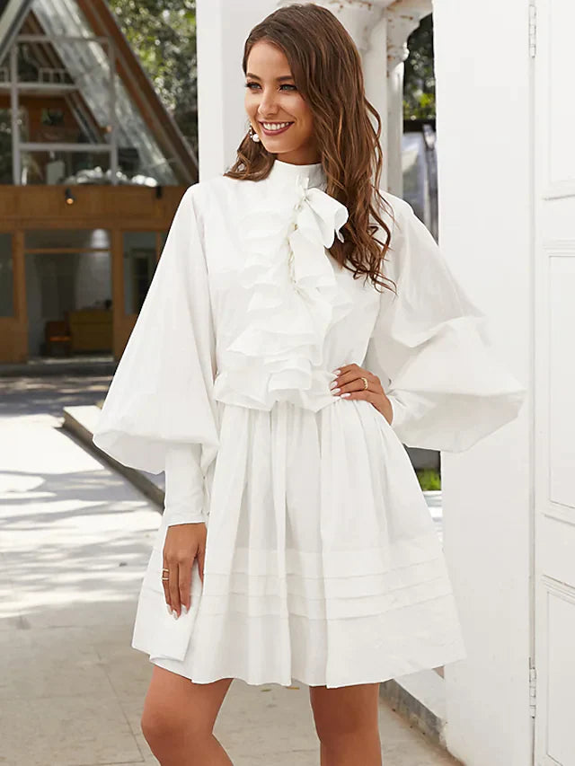 Woman wearing a dark A-line high neck long sleeve ruffled mini dress, front view.