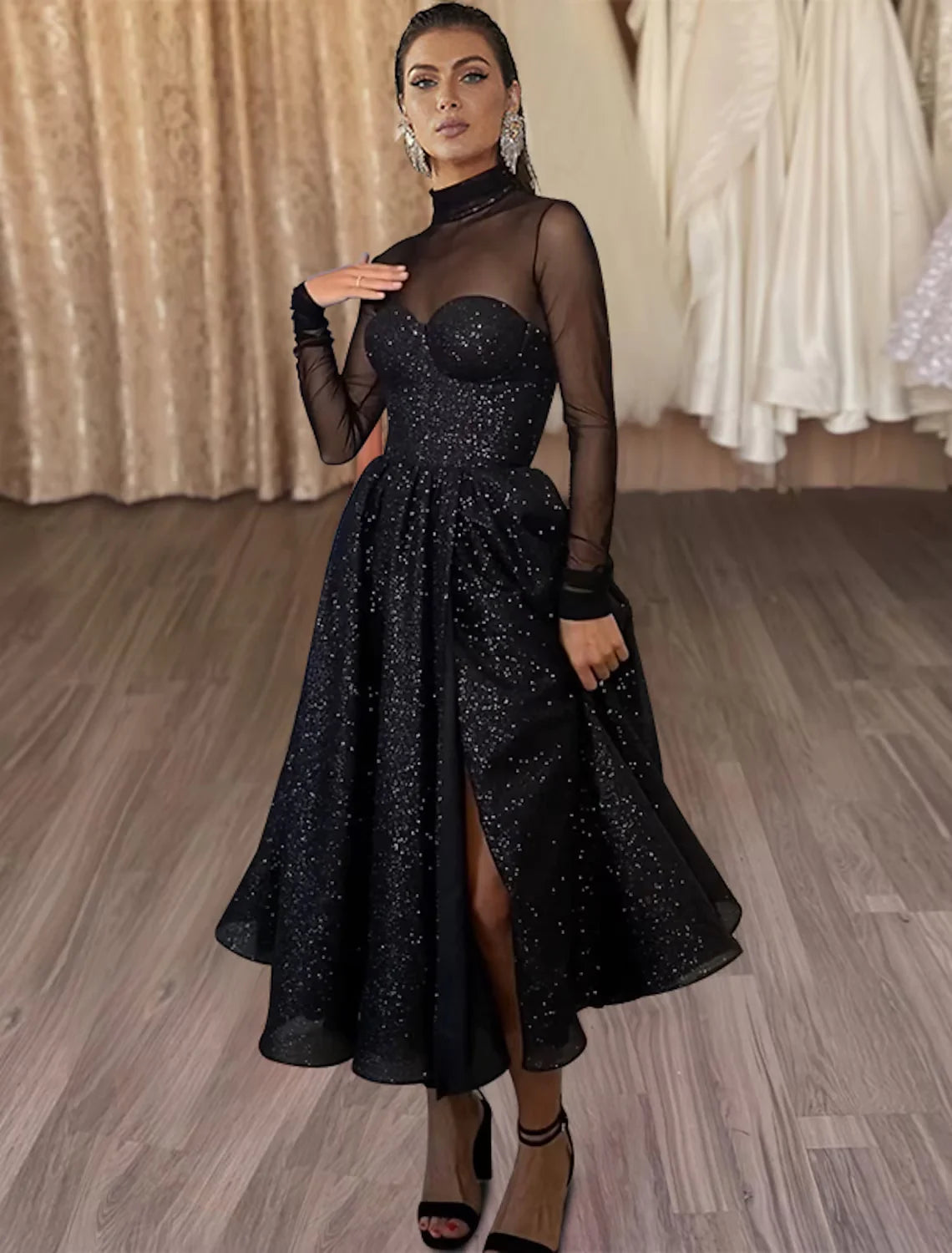 Model wearing an elegant A-line tea-length dress with long sleeves, high neck, and glitter tulle.