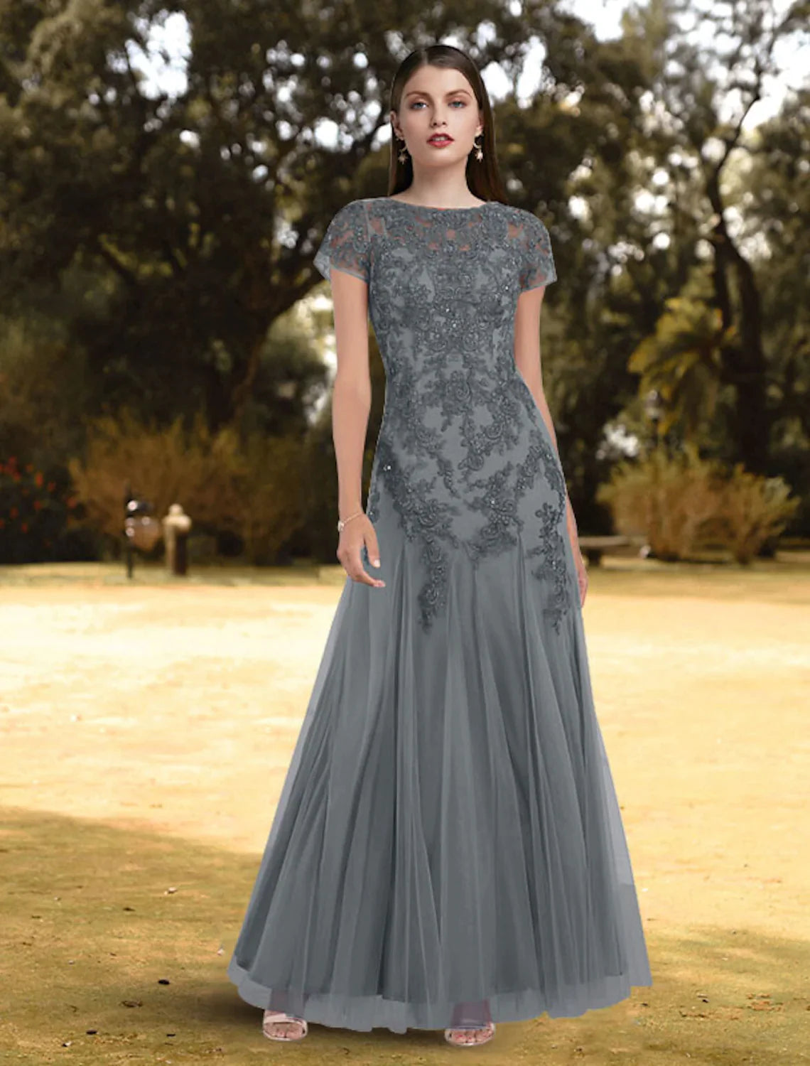 Full-length view of a woman wearing an elegant A-line jewel neck short sleeve lace pleated floor-length evening gown.