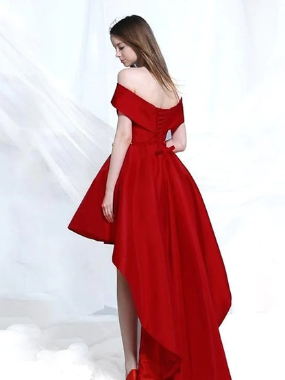 A woman posing in an elegant A-line off-shoulder satin cocktail dress with an asymmetrical hem.