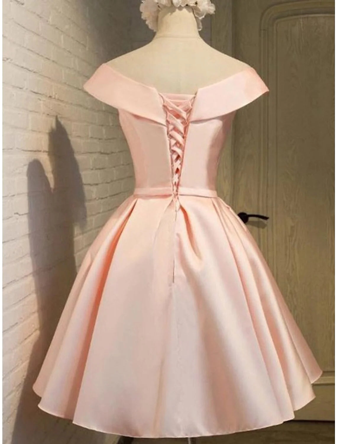 Back view of a woman in a pink off-shoulder A-line satin short dress with strappy details.
