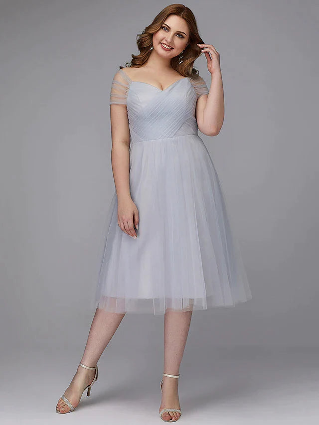 Model wearing a light-colored A-line off-shoulder tea length tulle dress with a sash ribbon and criss-cross back.