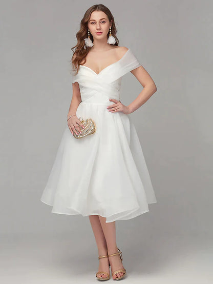 Model wearing an elegant white A-line off-shoulder tea-length cocktail dress with criss-cross pleats.