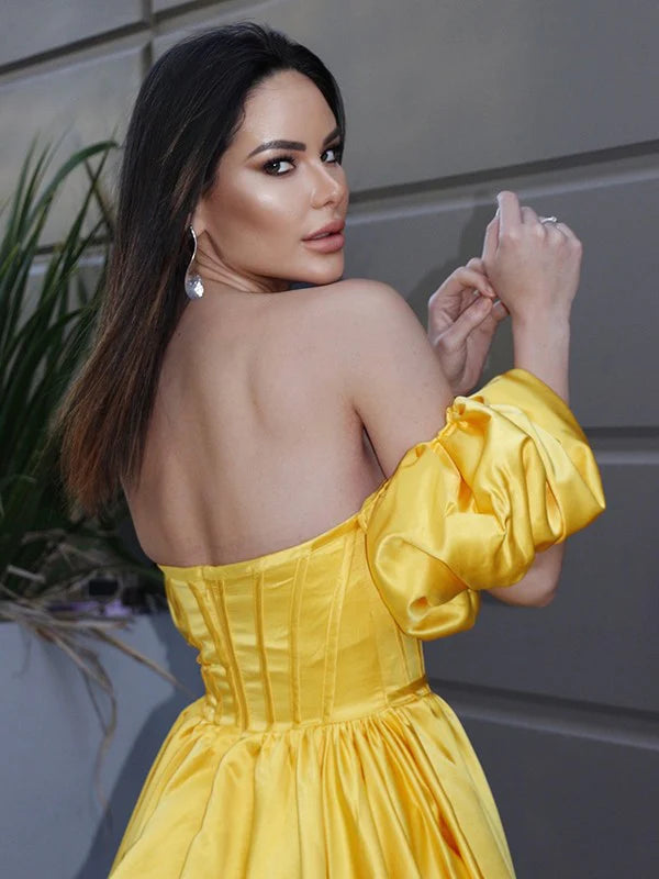 Back view of a flowing yellow A-line prom dress with a ruffled off-the-shoulder neckline.