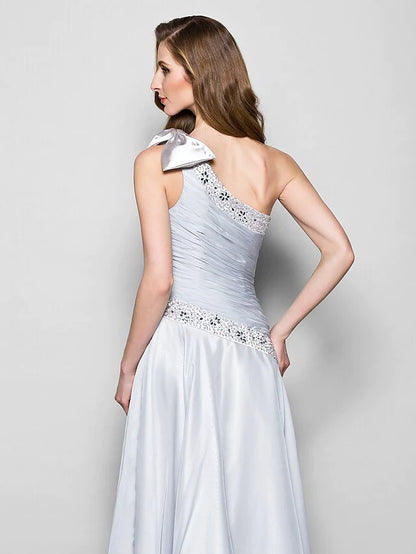 Close-up of the crystal beading and bow detail on the one-shoulder chiffon dress.