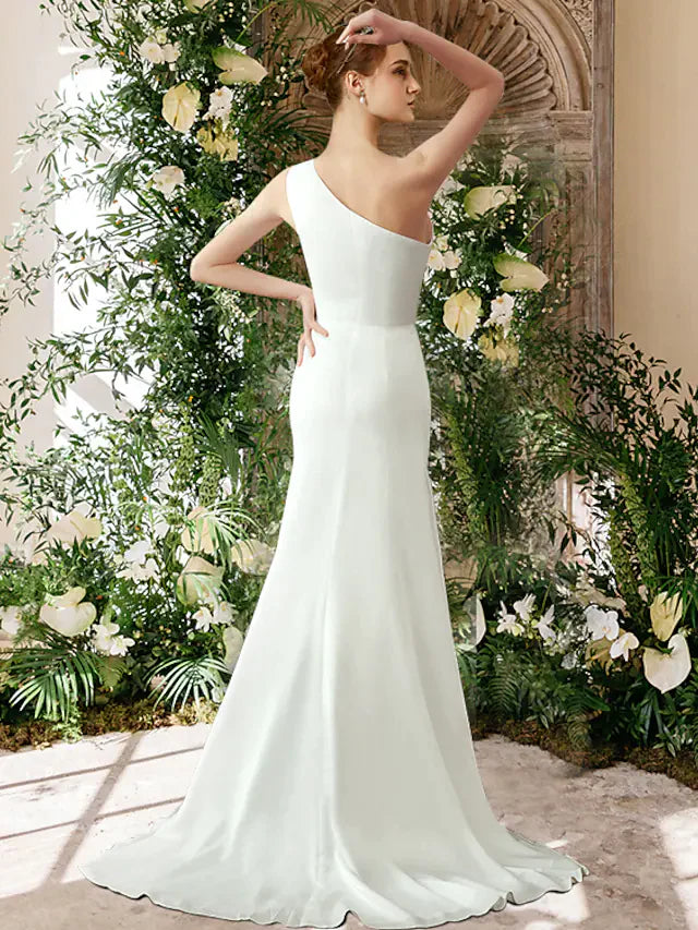Back view of a woman in a flowing white one-shoulder bridal gown.