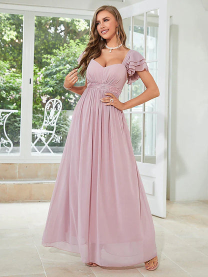 Woman posing in an elegant light blue A-line chiffon dress with square neck and short ruffled sleeves.