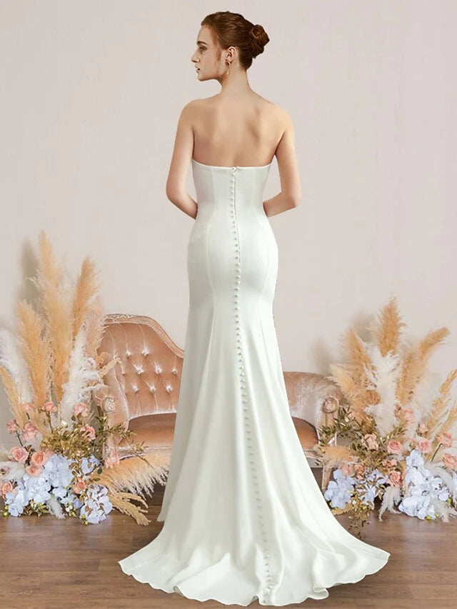 Back view of a woman in a simple white strapless backless wedding gown.