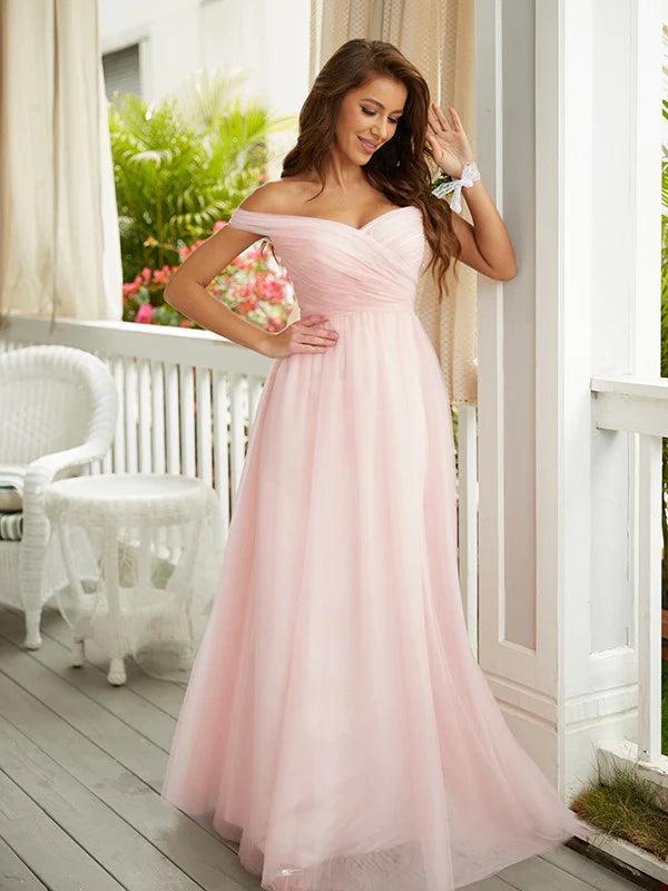 Woman in a light pink A-line off-shoulder tulle prom dress, standing elegantly.