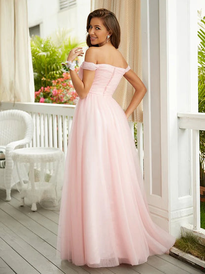 Woman in a light pink A-line off-shoulder tulle prom dress, posing from the side.