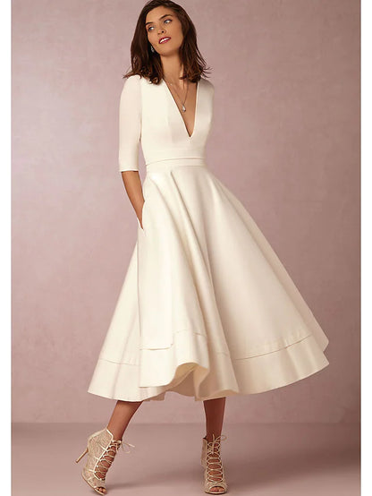Woman in a dark A-line V-neck half sleeve tea length dress with pleats and pockets.