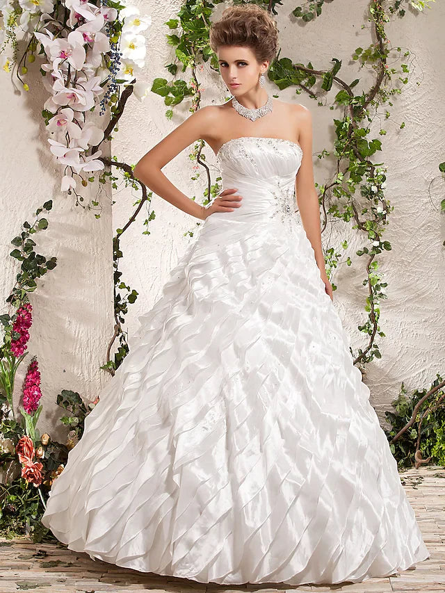 Model wearing a white strapless ball gown wedding dress with beading and ruffles.