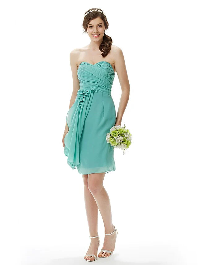 Woman wearing a light pink strapless knee-length chiffon bridesmaid dress with criss-cross draping and a flower detail.