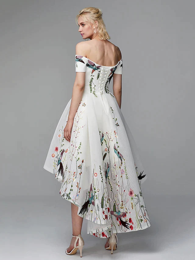 Side view of model wearing light blue floral embroidered off-shoulder high-low cocktail dress.