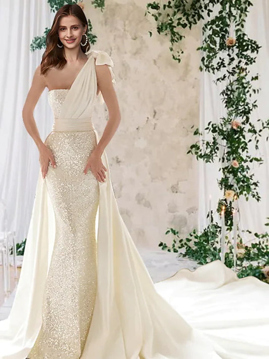 Model wearing an elegant one-shoulder white wedding dress with a sparkling sequined bodice and a flowing court train.