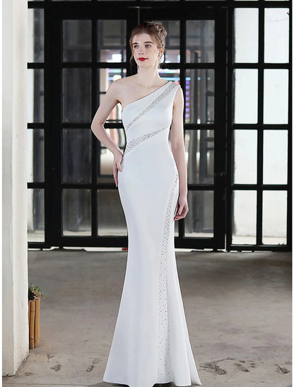 Woman wearing a one-shoulder mermaid evening gown with crystal details.