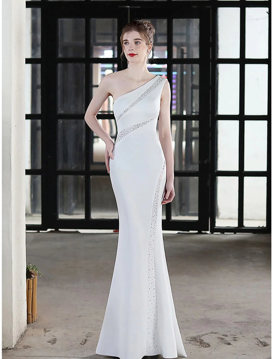 Woman wearing a one-shoulder mermaid evening gown with crystal details.