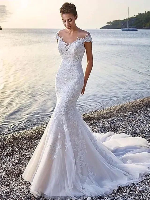 Model wearing an elegant white organza wedding dress with a scoop neck, appliques, and court train.