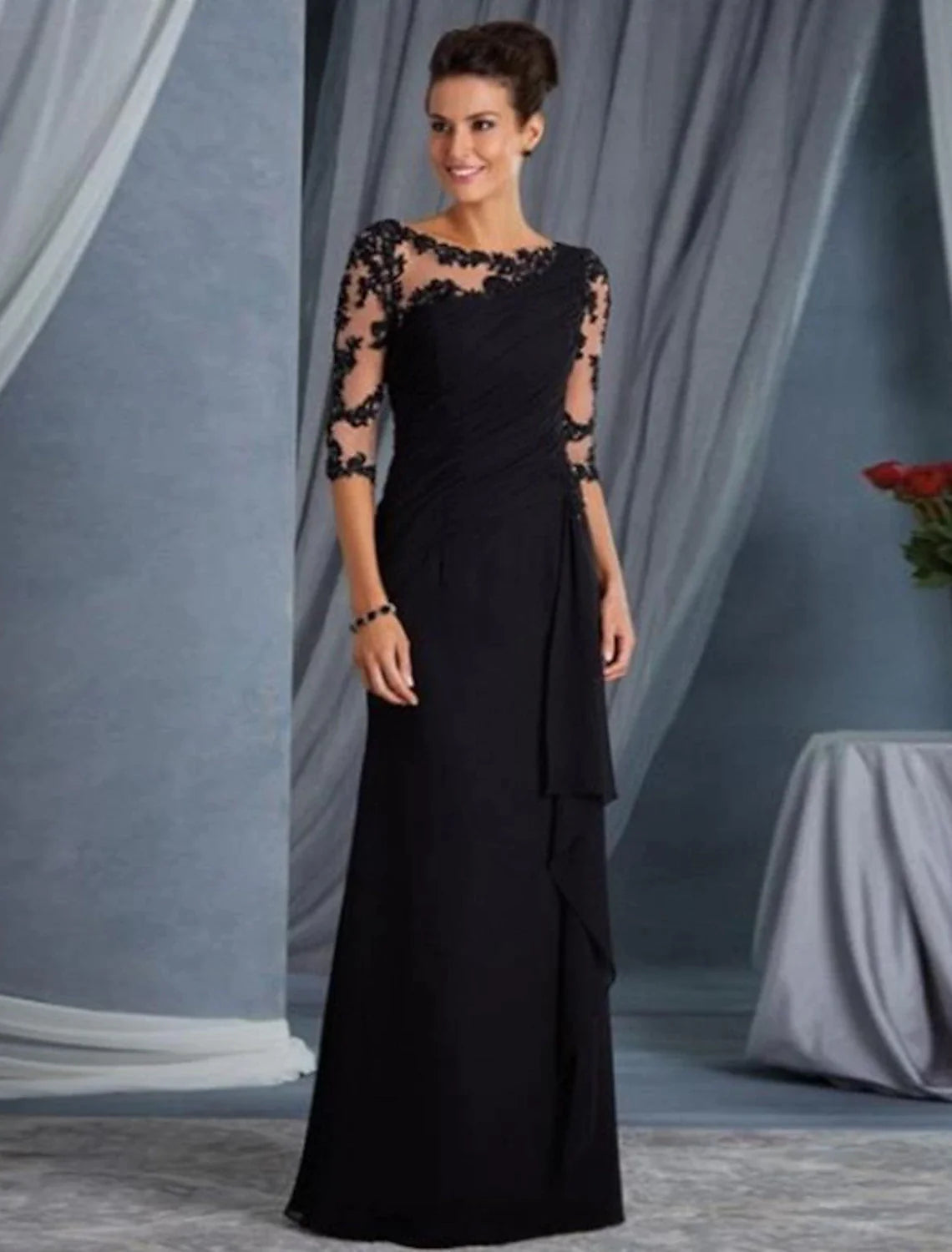 Woman wearing a black sheath evening gown with half sleeves and a jewel neck.