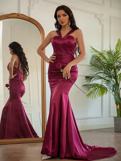 Woman wearing a long silk-like satin ruched halter prom dress, front view.