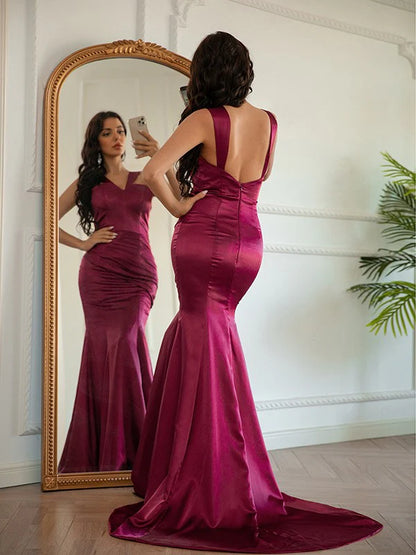 Side view of a woman in a long silk-like satin ruched halter prom dress.