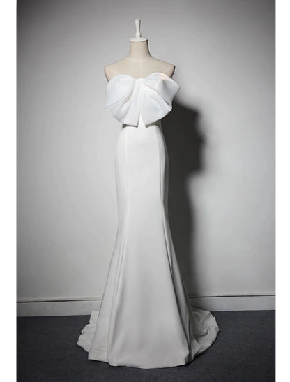 Woman in an elegant strapless mermaid trumpet evening gown with bows and a sweep train.