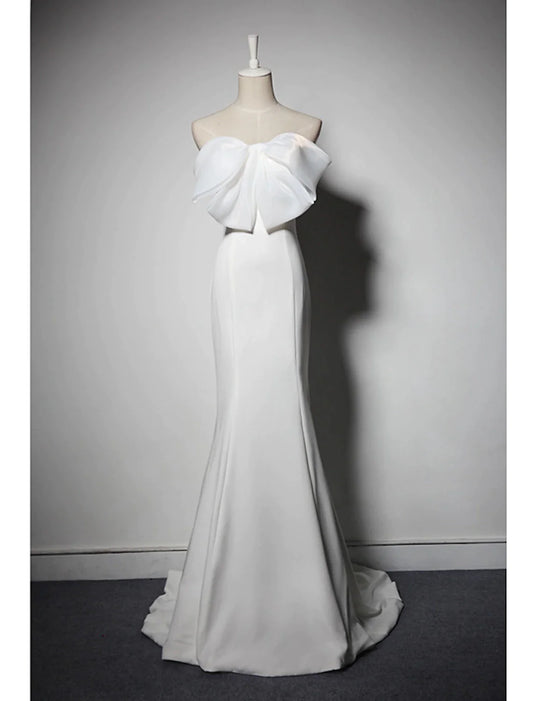Woman in an elegant strapless mermaid trumpet evening gown with bows and a sweep train.