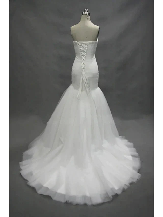 Back view of a model wearing a white strapless sweetheart tulle wedding dress with ruched details and a flowing court train.
