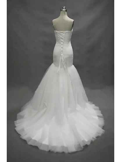 Back view of a model wearing a white strapless sweetheart tulle wedding dress with ruched details and a flowing court train.