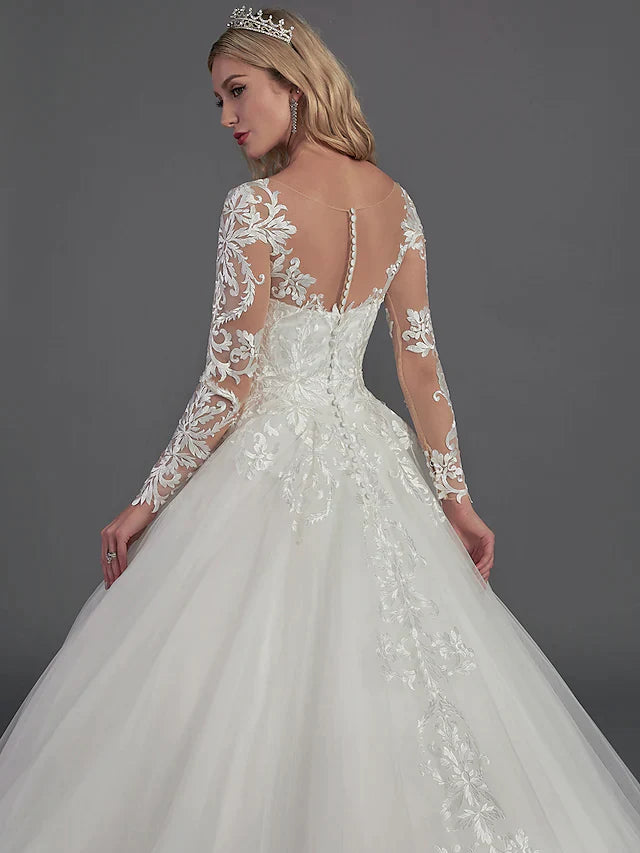 Bride posing in the ball gown wedding dress, emphasizing the flowing tulle skirt and long lace sleeves.