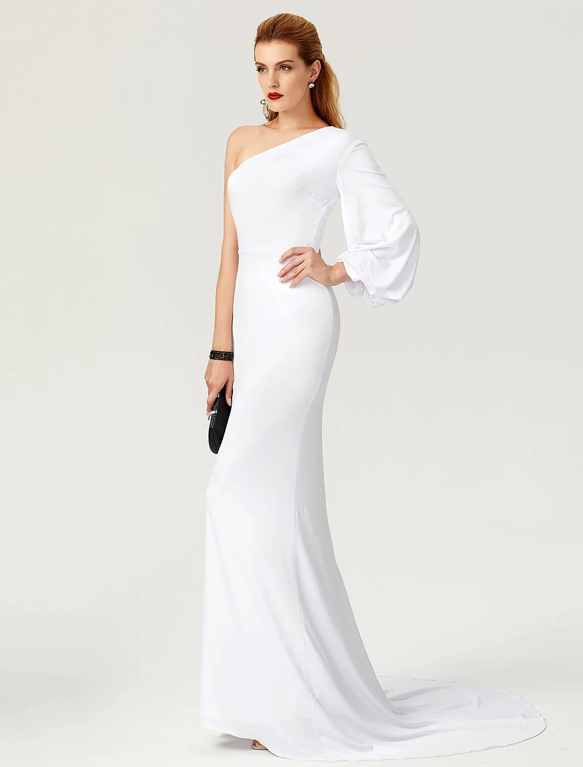 Full-length view of a woman in a dark mermaid trumpet gown with one long sleeve and pleats.