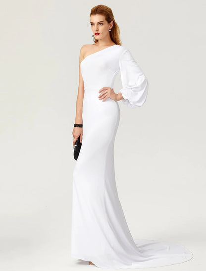 Full-length view of a woman in a dark mermaid trumpet gown with one long sleeve and pleats.
