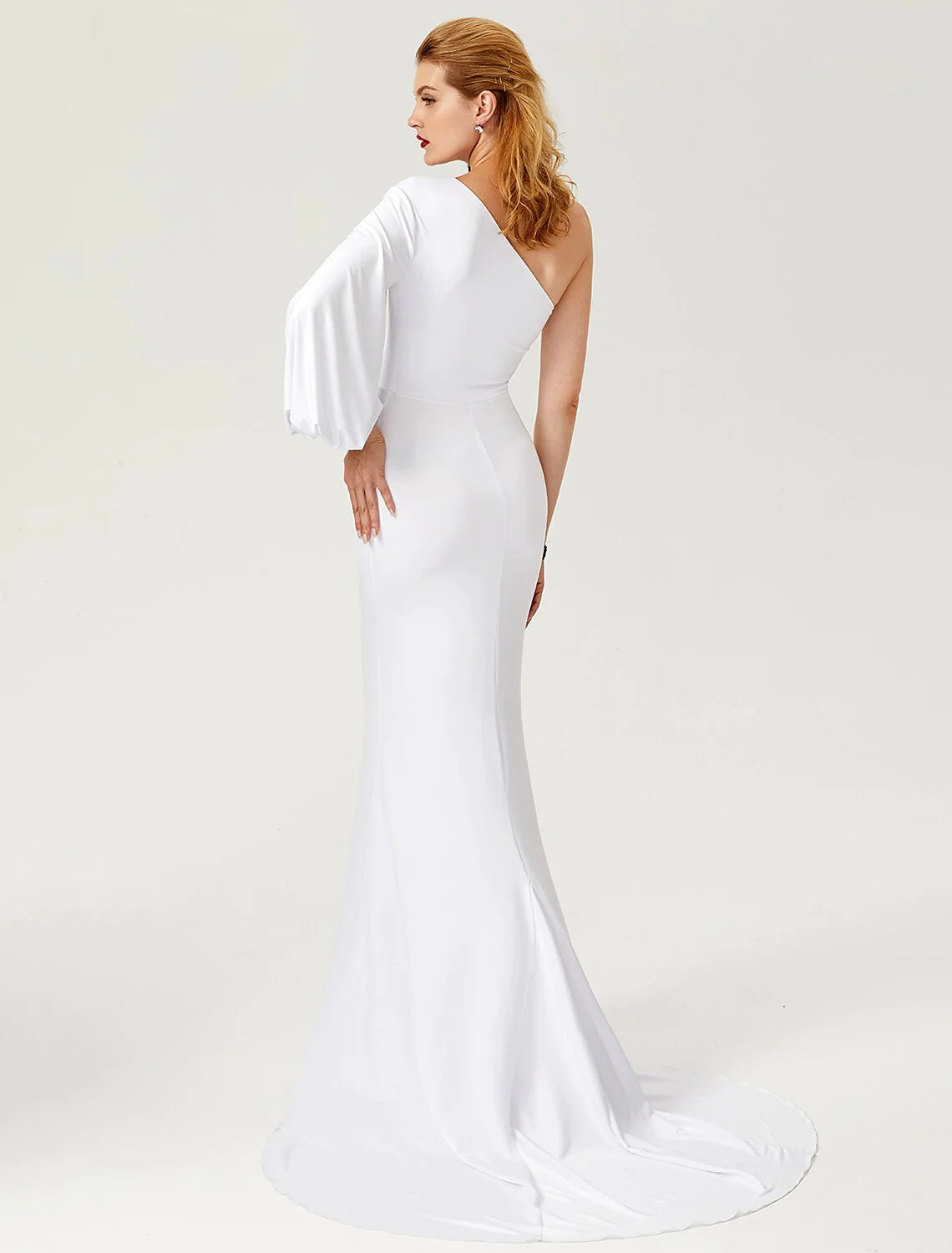 Side view of a woman in a dark one-shoulder long sleeve mermaid gown, showing the court train.