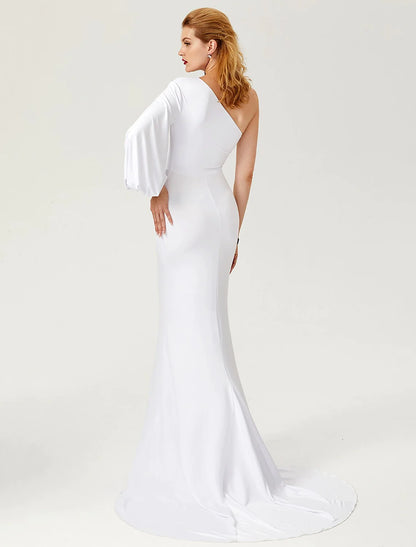 Side view of a woman in a dark one-shoulder long sleeve mermaid gown, showing the court train.