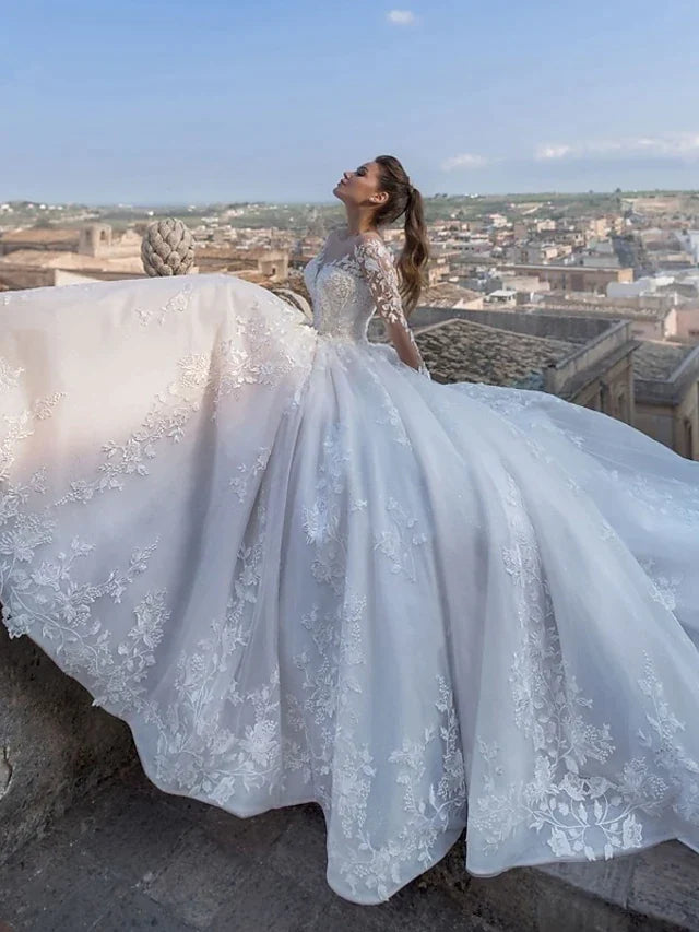 Bride wearing a glamorous V-neck ball gown wedding dress with long lace illusion sleeves and a chapel train.