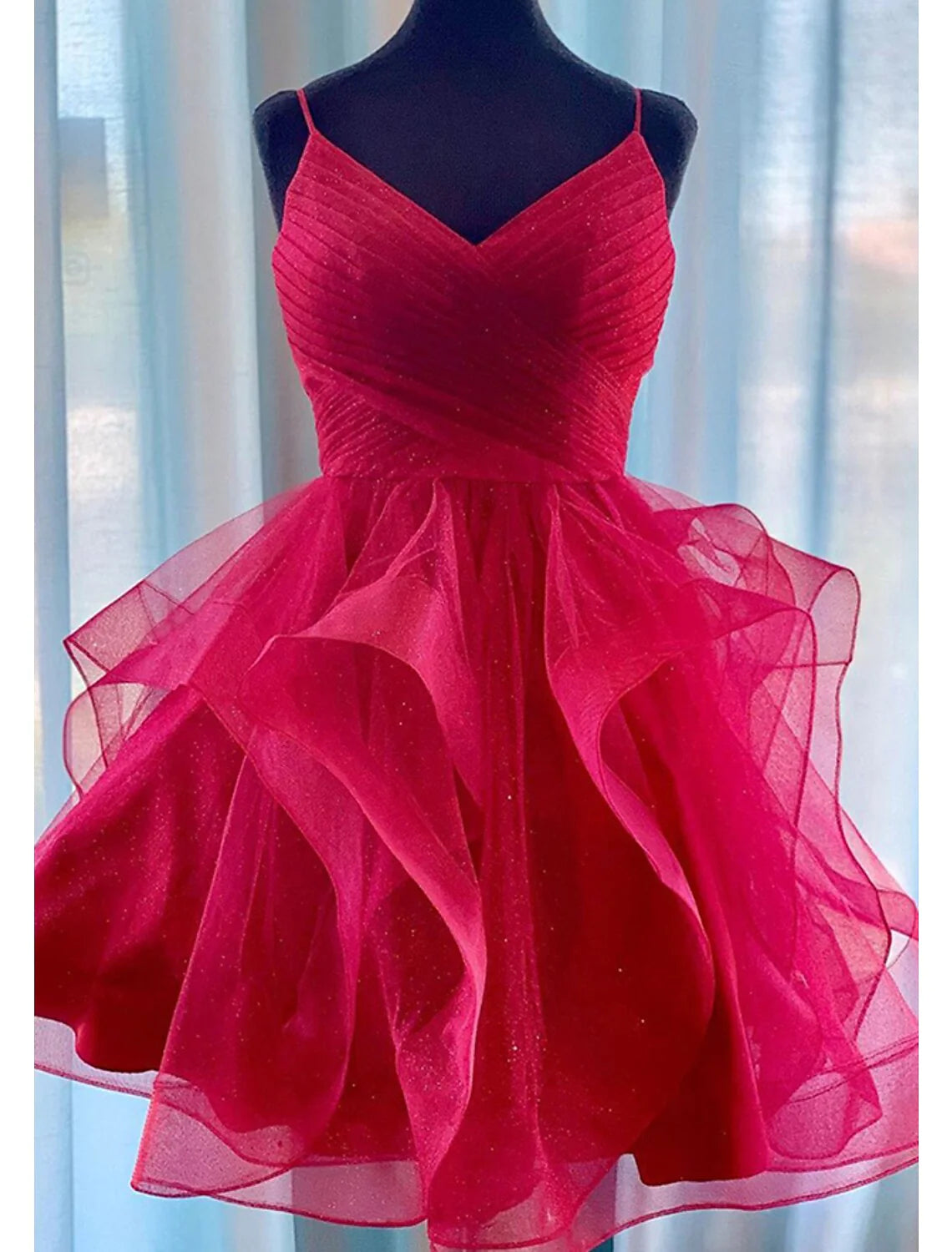 Woman wearing a shimmering A-line tiered plisse short homecoming dress with spaghetti straps.