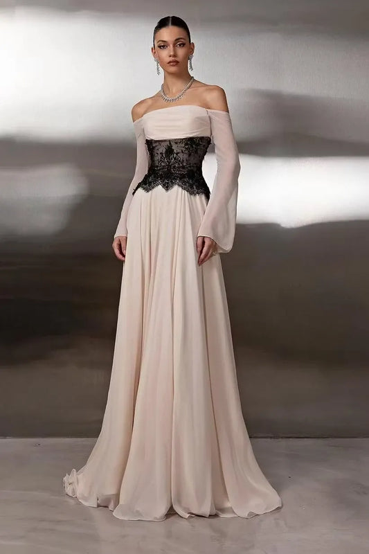Woman wearing a nude A-line off-shoulder prom dress with black lace corset and sheer long sleeves.