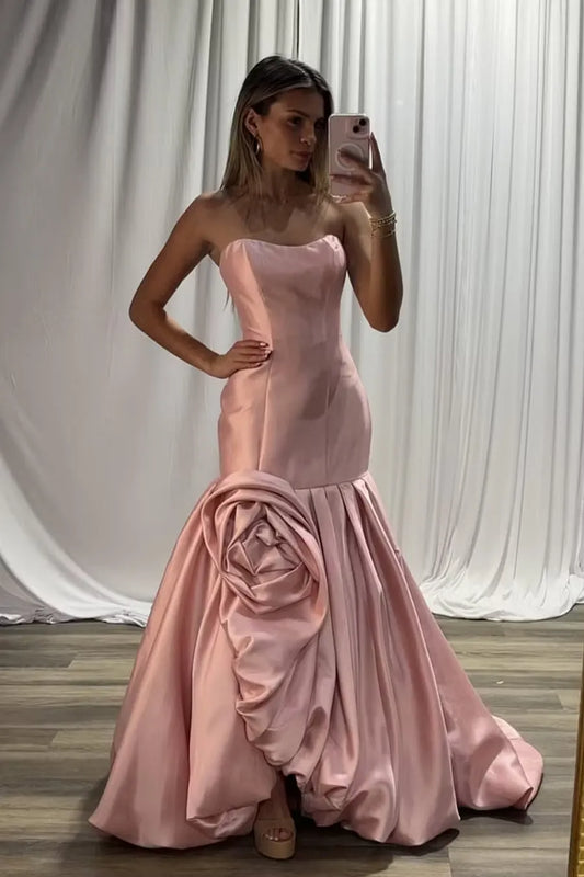 Woman in a pink strapless mermaid prom dress with a large 3D rose appliqué on the hip.