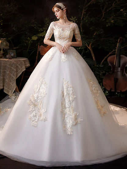 Bride wearing a white princess ball gown wedding dress with jewel neck, short sleeves, lace appliques, and chapel train.