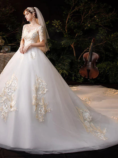 Close-up of the bodice of a white wedding dress, showing jewel neck, short sleeves, and intricate lace appliques.