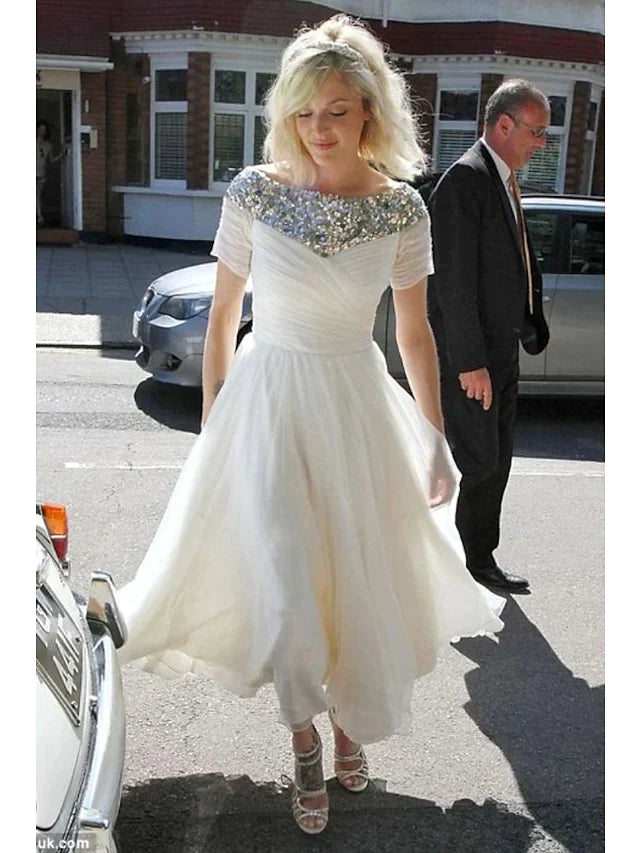 Model wearing a white A-line tea-length wedding dress with jewel neck and short sequined sleeves.
