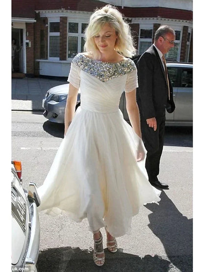 Model wearing a white A-line tea-length wedding dress with jewel neck and short sequined sleeves.